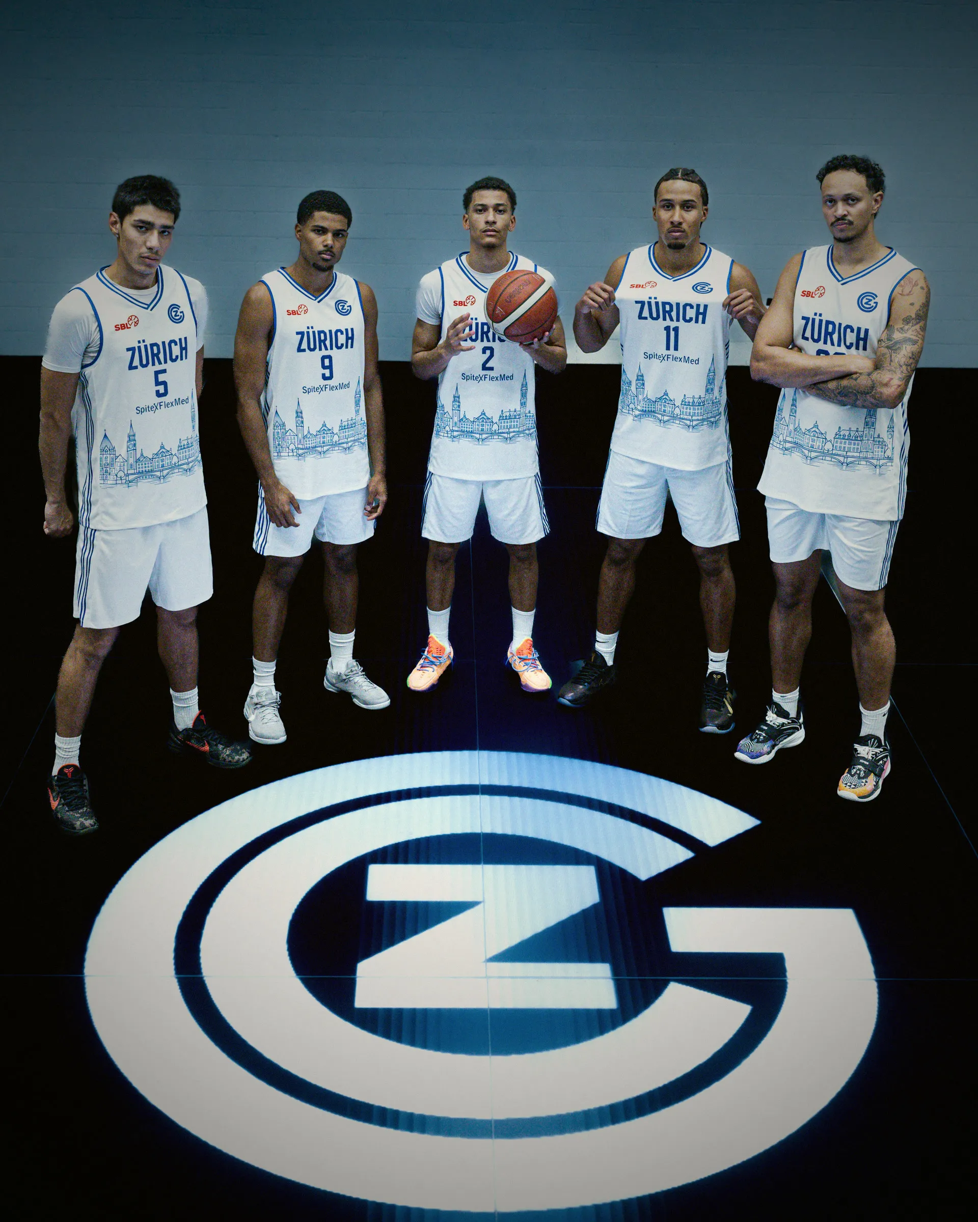 Fünf Spieler von GC Basketball im weissen Heimtrikot stehen auf dem beleuchteten GC-Logo im dunklen Studio