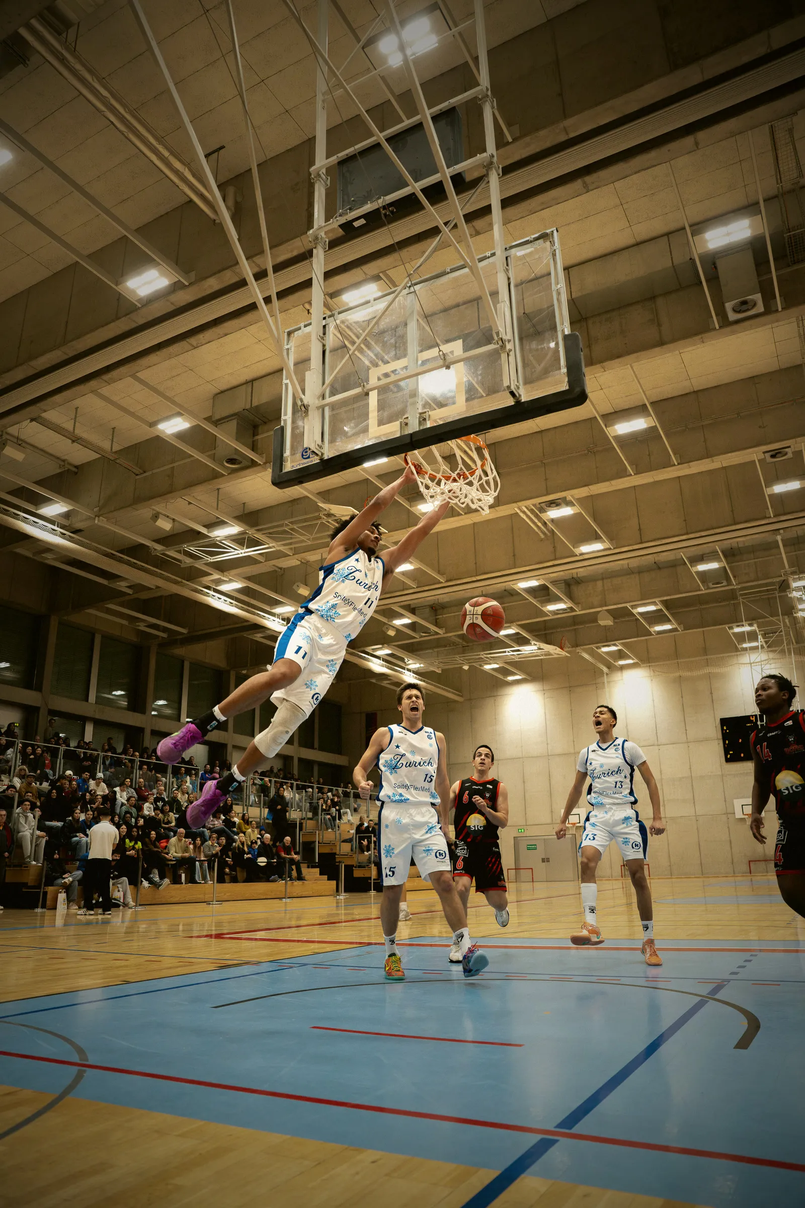 Christmas Game, Spieler mit der Nummer 11 im weissen Weihnachtstrikot mit Schneeflocken hängt nach einem Dunk am Korb